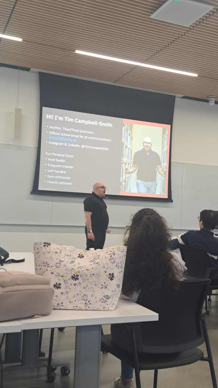 Professor Tim standing in front of a screen displaying his picture and introduction, while addressing a filled classroom of students
