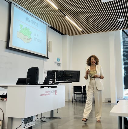 Woman presenting in a classroom setting, gesturing with her hands while speaking to an audience