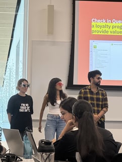 3 students are standing in front of the class, one girl on the left, one girl in the middle and one boy in the right. They all are wearing different types of sunglasses. 