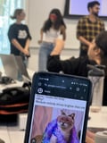 A cat meme on the phone, the cat is wearing red glasses, three people with glasses with the background, one wearing the same red glasses as the cat 