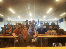 Professor Leigh posing for a picture with students in a lively classroom setting.