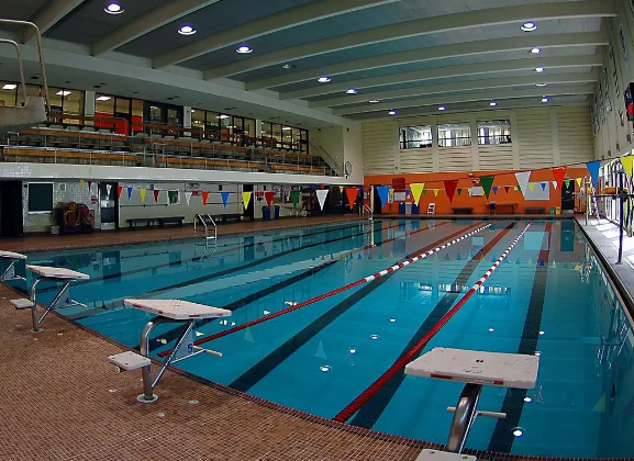 A large indoor swimming pool. The room is well illuminated with lights. There are colorful little flags above the pool tied with a string. 