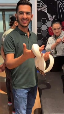 A boy with spectacles wearing green T shirt and denims holding a white python. 