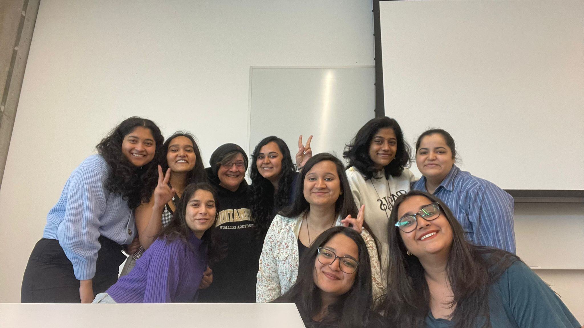 Students smiling and posing for pictures with their professor in the middle.