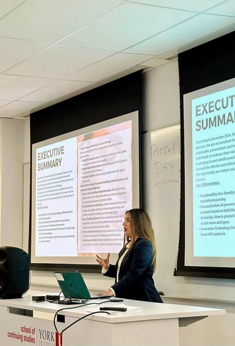 The author in professional attire is giving a presentation in the background, laptop on the desk with speaker on her right