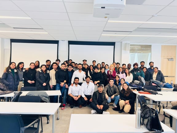 Classmates and their professor gather in a classroom, posing cheerfully for a group photograph.