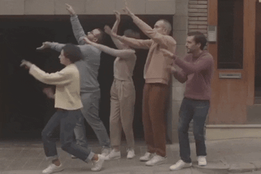 Group of 5 people waving their hands on a sidewalk in front of a building