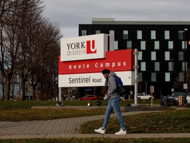 Student Walking by the Keele Campus York Sign. 