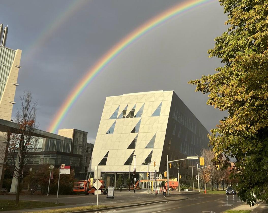  Two students are standing at a whiteboard in a classroom at york university scs, engaging in a collaborative activity. The slide on the screen above them displays instructions for an in-class branding activity, asking students to analyze a brand they think is good. The ceiling features wooden slats, and the room has a modern design. The students are writing notes related to a brand named 